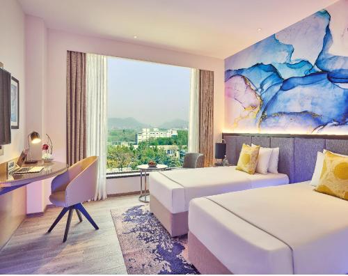 a hotel room with two beds and a desk and a window at Vivanta Navi Mumbai Turbhe in Navi Mumbai