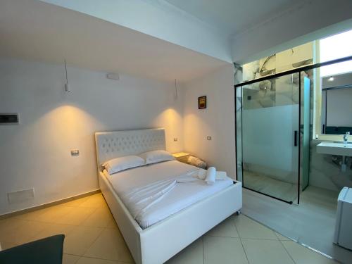 een slaapkamer met een wit bed en een glazen douche bij Hotel Kristal Borsh in Borsh