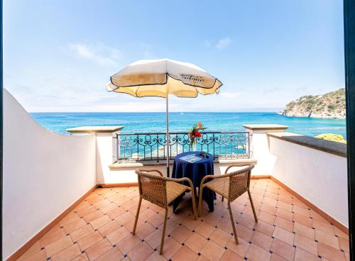 uma mesa e cadeiras com um guarda-sol e o oceano em Hotel Terme Tritone Resort & Spa em Ischia
