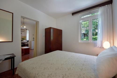a white bedroom with a bed and a window at Apartmani Kuća u maslinama in Sveti Stefan