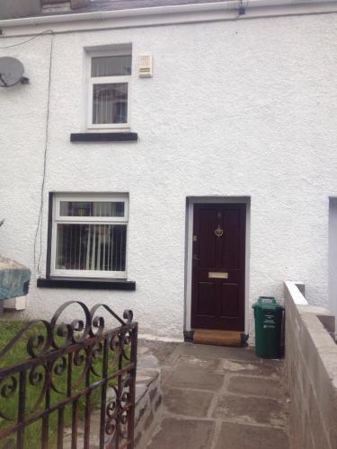 a white house with a black door and a fence at Honeycomb Cottage in Aberdare