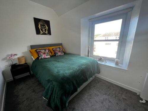 a bedroom with a bed with a green comforter and a window at Cozy and modern flat in the heart of Hawick in Hawick