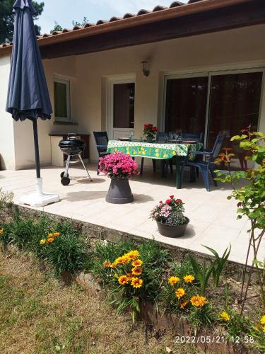 eine Terrasse mit einem Tisch, einem Sonnenschirm und Blumen in der Unterkunft Maison les Mathes in Les Mathes