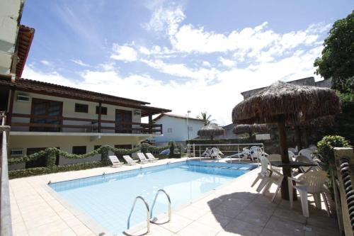 a swimming pool with chairs and a table and an umbrella at Hotel Pousada Guayporã in Guarapari