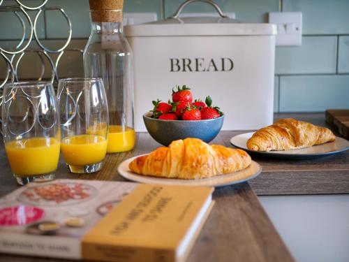 a table with bread and a bowl of strawberries and glasses of orange juice at Padstow Escapes - Breakers Holiday Cottage in St Merryn