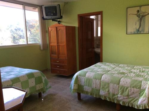a bedroom with two beds and a tv on the wall at Casa de Huéspedes La Rosa in Ixtapan de la Sal