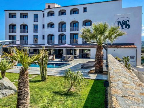a hotel with palm trees in front of a building at Maria Stella in LʼÎle-Rousse