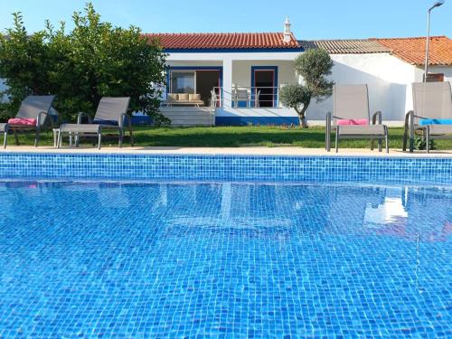 a blue swimming pool with two chairs and a house at Casa Citrus Limão - Between the Hills & the Ocean in Silves