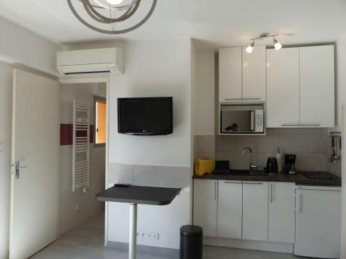 Il comprend une cuisine avec des placards blancs et une télévision murale. dans l'établissement Charmant studio climatisé avec balcon à 50m de la plage - Le Lavandou centre-ville - FR-1-308-110, au Lavandou