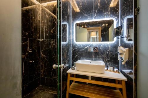 een zwart betegelde badkamer met een wastafel en een spiegel bij GIARDINO High living suites in Drama