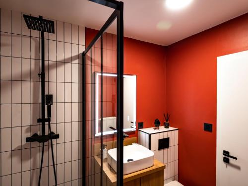 uma casa de banho com paredes vermelhas, um lavatório e um chuveiro em Élégant studio à côté du Parlement em Estrasburgo