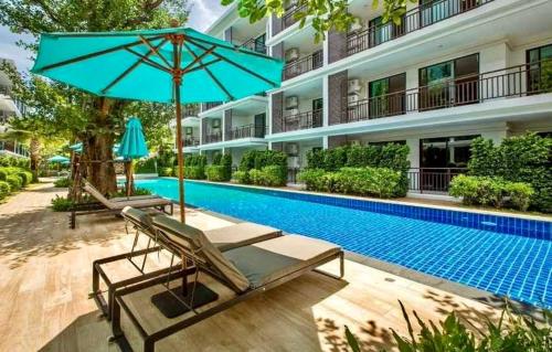 a swimming pool with a blue umbrella and chairs next to a building at The Title Rawai: Beachfront condotel in Rawai Beach