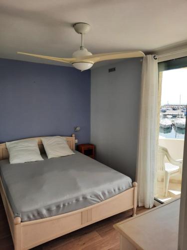 Cet appartement comprend une chambre dotée d'un lit avec un mur bleu et une fenêtre. dans l'établissement Au Barcarès, vue magnifique sur le port et la mer, au Barcarès