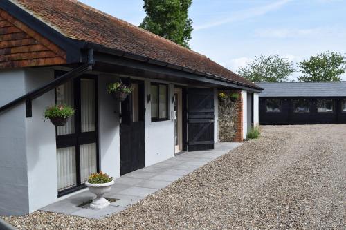 a cottage with a black door and a gravel driveway at Sandhurst Farm Forge Self Catering Stableblock in Sittingbourne