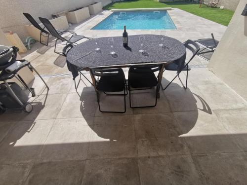 une table avec des chaises et une bouteille de vin dessus à côté d'une piscine dans l'établissement Villa calme piscine proche mer petite salle cinéma, à Montagnac