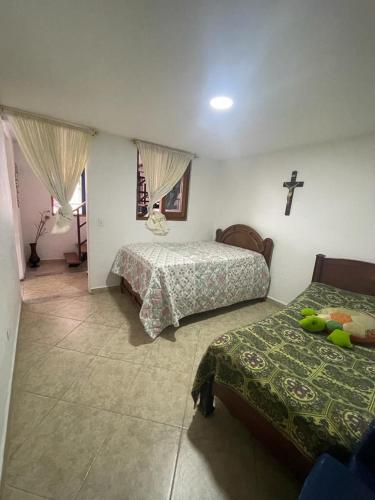een slaapkamer met 2 bedden en een kruis aan de muur bij Villa Chela, Hermosa casa de descanso, Venecia Antioquia in Venecia