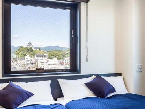 a bed with blue and white pillows and a window at HOTEL LiVEMAX Kakegawa-Ekimae in Kakegawa