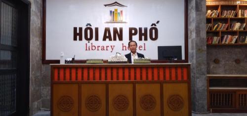 a man standing behind a counter in a library at Hoi An Pho Library Hotel in Hoi An