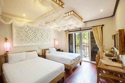 a bedroom with two beds and a desk and a window at Hoi An Pho Library Hotel in Hoi An