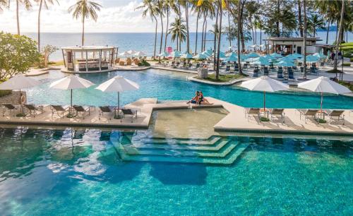 a swimming pool with chairs and umbrellas and the ocean at SAii Laguna Phuket in Bang Tao Beach