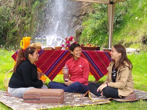 three women sitting on a picnic blanket in front of a waterfall at Fundo El Chocho in Cajamarca