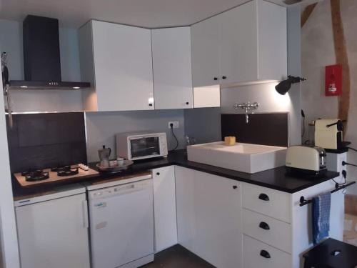 eine Küche mit weißen Schränken, einer Spüle und einer Mikrowelle in der Unterkunft St Elme, maison de pêcheurs, WIFI jardin in Ault