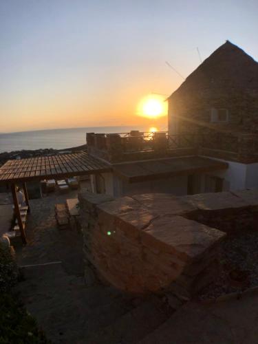 a sunset over a building with the ocean in the background at The Stone Windmill in Koundouros