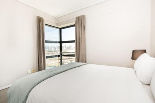 a white bedroom with a bed and a window at Durban Point Waterfront, 1006 Quayside in Durban