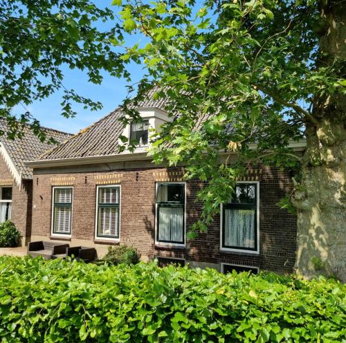 an old brick house with windows and a tree at Het Voorhuis boerderij Hoeve Vrede Best in Weesp