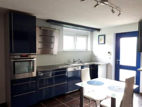 cocina con armarios azules, mesa, mesa y comedor en Lovely Appartment with private patio and private entrance in Luxembourg 60m2, en Saeul