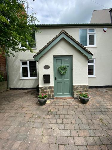 a house with a green door and two plants at Stoop Cottage - in the heart of Quorn in Quorndon