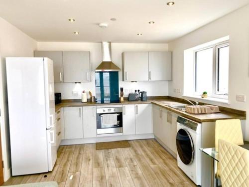 a kitchen with white cabinets and a white refrigerator at Lovely New 2 Bedroom Condo with Stunning Seaviews in Penmaen-mawr