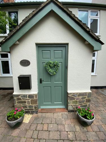 a green door on a house with two flower pots at Stoop Cottage - in the heart of Quorn in Quorndon