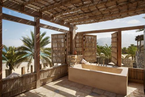 La salle de bains est pourvue d'une baignoire sur le balcon avec des palmiers. dans l'établissement Six Senses Zighy Bay, à Dibba