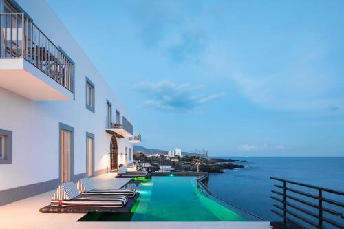 a swimming pool with lounge chairs and the ocean at White Exclusive Suites & Villas in Lagoa