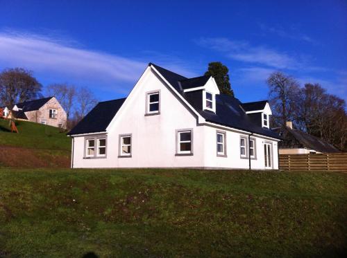a white house with a black roof on a hill at Highland Farm Cottages in Dingwall
