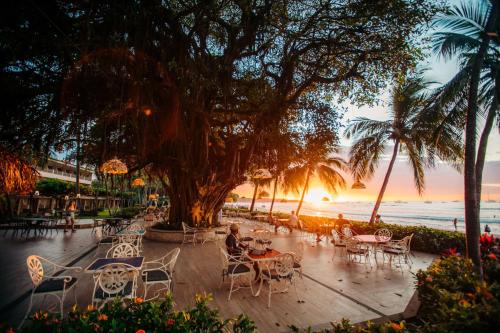 eine Gruppe von Tischen und Stühlen am Strand bei Sonnenuntergang in der Unterkunft Hotel Tamarindo Diria Beach Resort in Tamarindo