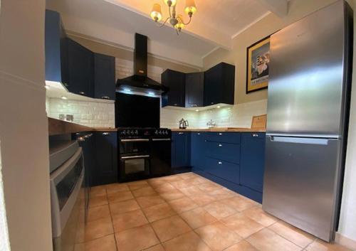 a kitchen with blue cabinets and a stainless steel refrigerator at Granary at Kergudon Gîtes, family gîte with pool in Sizun