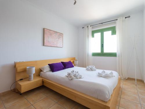 a bedroom with a bed with white sheets and purple pillows at HomeForGuest Apartamento con Piscina en Caleta de Fuste in Caleta De Fuste