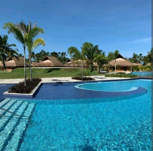 a swimming pool with blue water and palm trees at Eco Resort Praia dos Carneiros - Flats & Bangalô - LocarHouse in Tamandaré