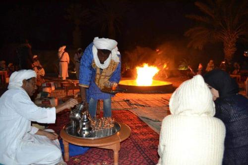 un grupo de personas de pie alrededor de una estatua delante de un fuego en Riad gnaoua khamlia en Merzouga