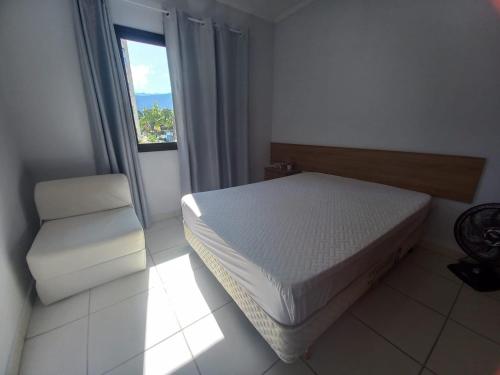 a bedroom with a bed and a chair and a window at Lindo apartamento com vista para o mar em Caraguá! in Caraguatatuba