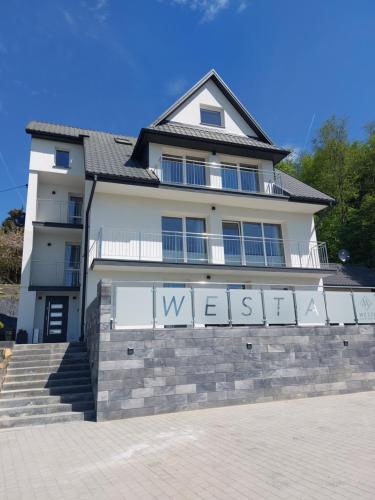 a white house with a sign on a wall at Westa Apartamenty in Krynica Zdrój