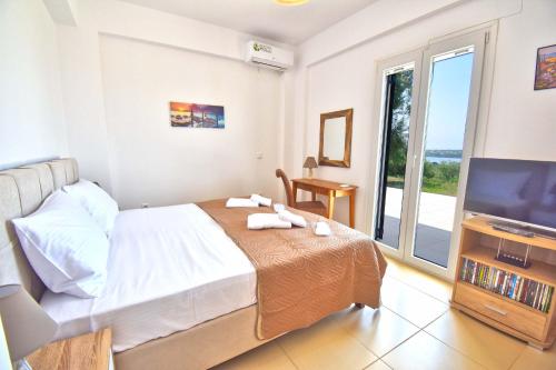 a bedroom with a bed and a tv and a balcony at Villa Menethea Sea View - 5min from Issos beach in Línia