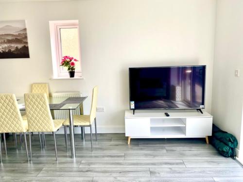a living room with a tv and a table with chairs at Lovely New 2 Bedroom Condo with Stunning Seaviews in Penmaen-mawr