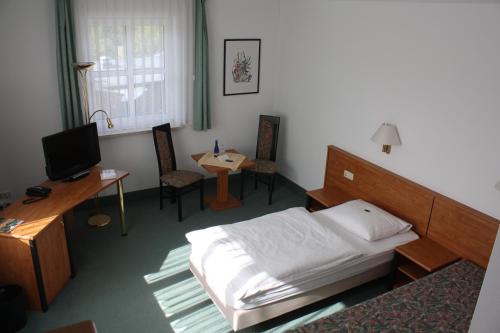 a bedroom with a bed and a desk and a television at Hotel & Restaurant Bergfried in Saalfeld
