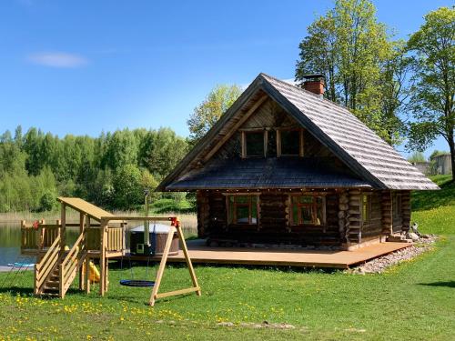 a log cabin with a deck and a playground at Vucini in Andzeļi