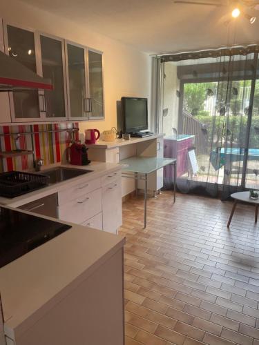 een keuken met witte kasten en een tafel met een televisie bij Appartement avec jardin Gruissan in Gruissan