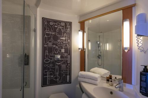 La salle de bains est pourvue d'un lavabo, d'une douche et d'un miroir. dans l'établissement IBIS Cannes Mouans Sartoux Piscine parking gratuit, à Mouans-Sartoux
