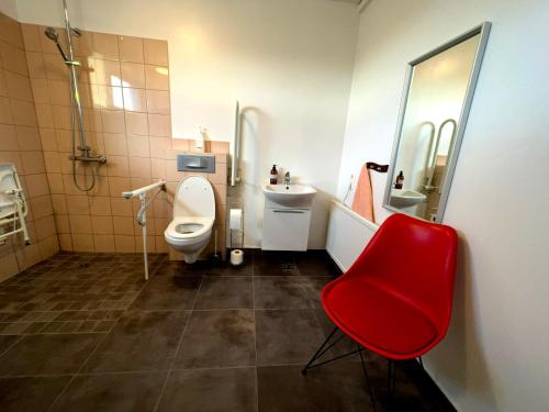 a bathroom with a toilet and a sink and a red chair at Bakland ad Lágafelli Apartment in Búðarhólshverfi